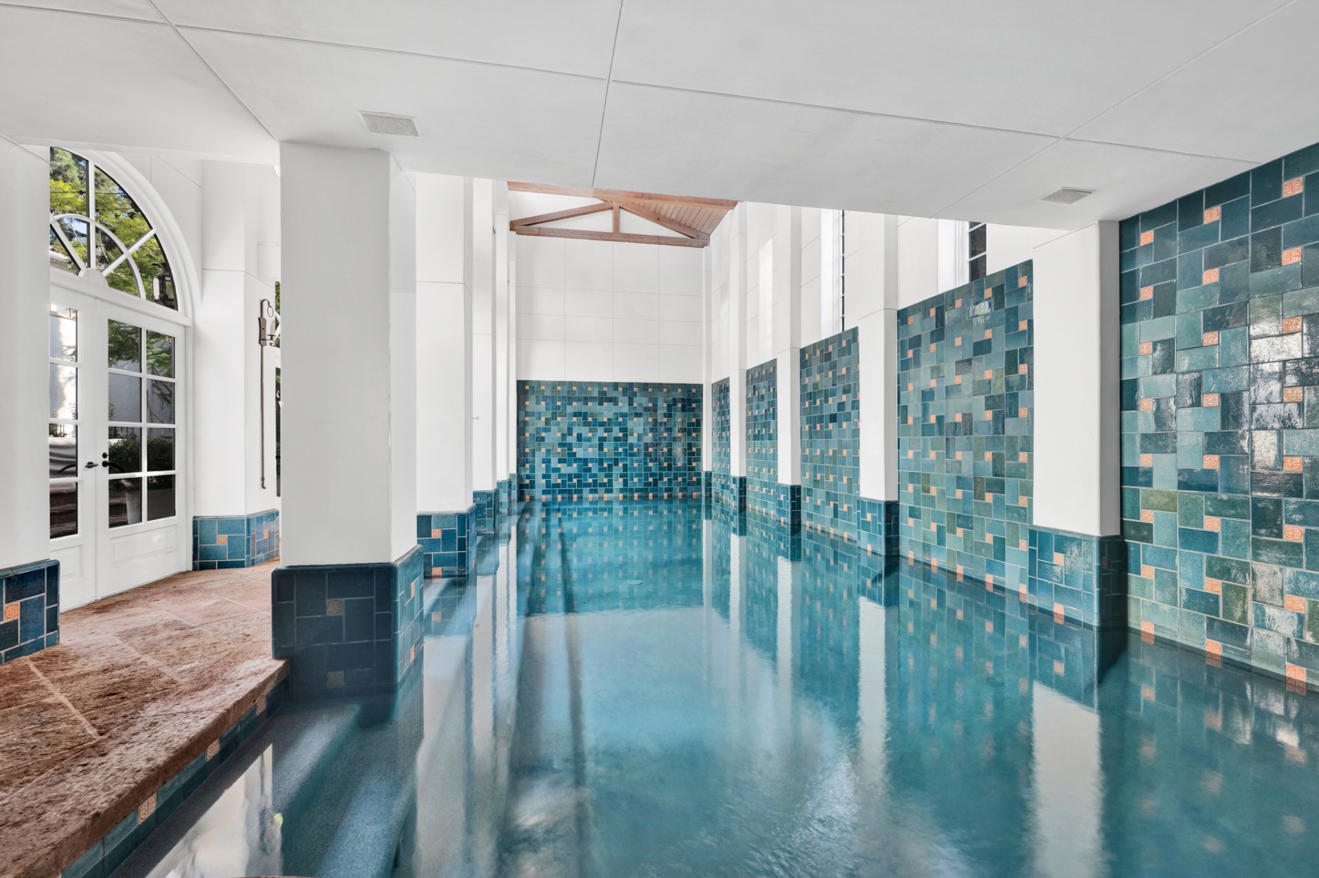 Indoor pool with arched French doors opening to the garden