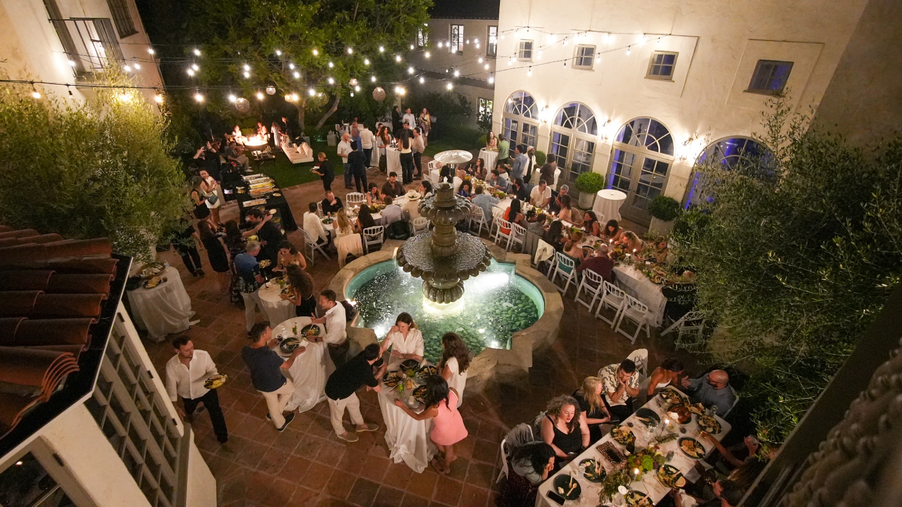 Guests dining around the fountain at night under string lights